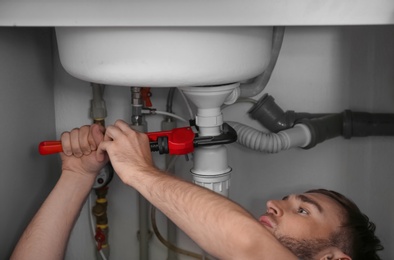 Photo of Professional plumber fixing sink with pipe wrench, closeup