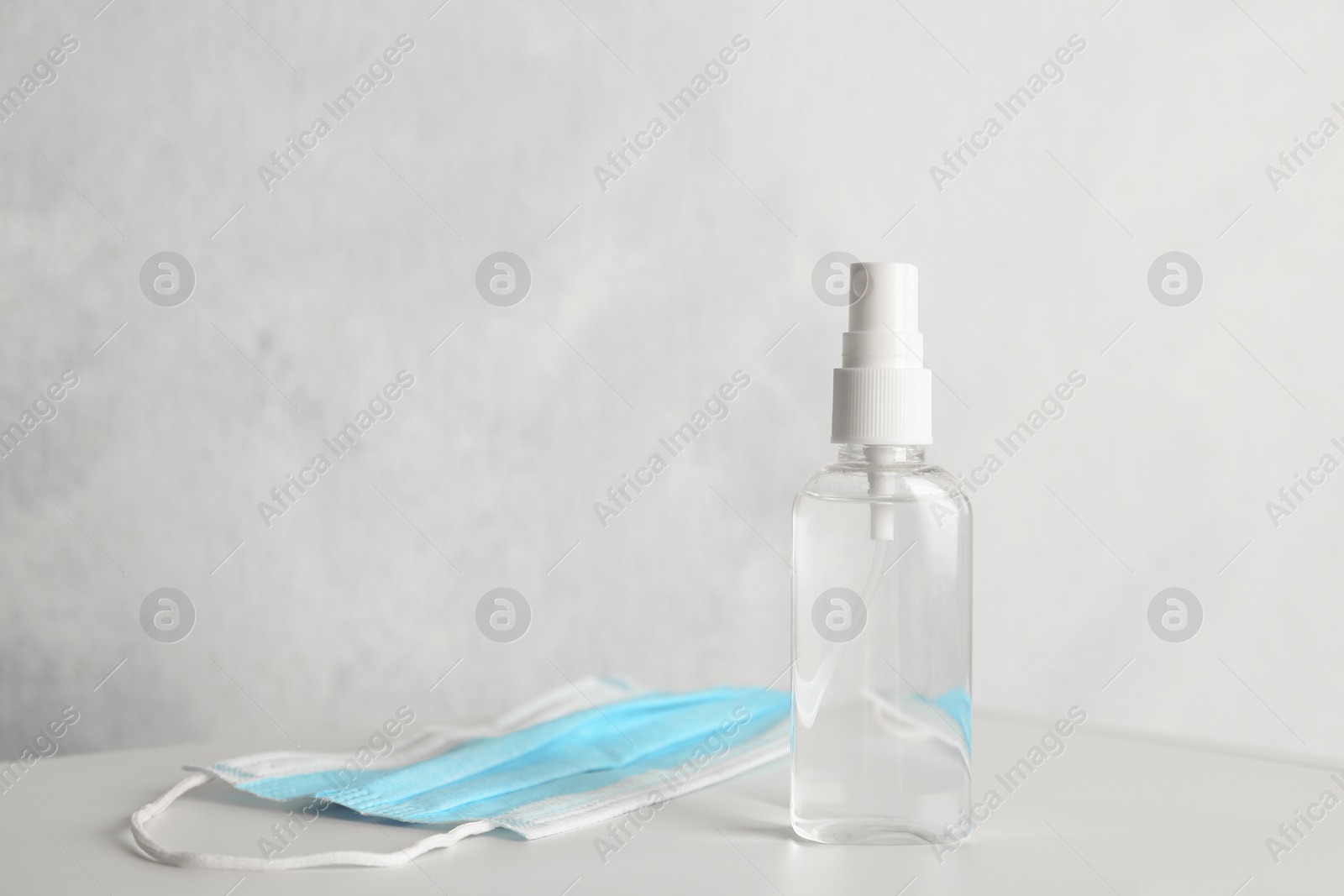 Photo of Antiseptic spray and protective mask on table against light background. Protection from virus