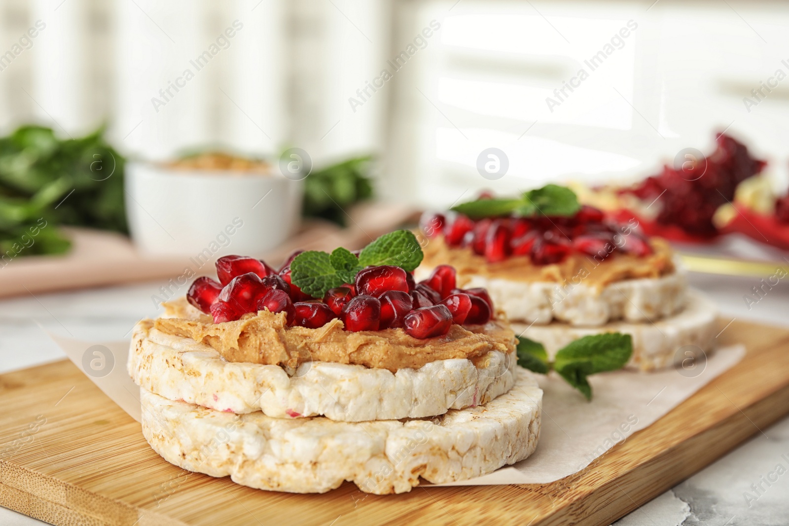 Photo of Puffed rice cakes with peanut butter, pomegranate seeds and mint on wooden board, closeup