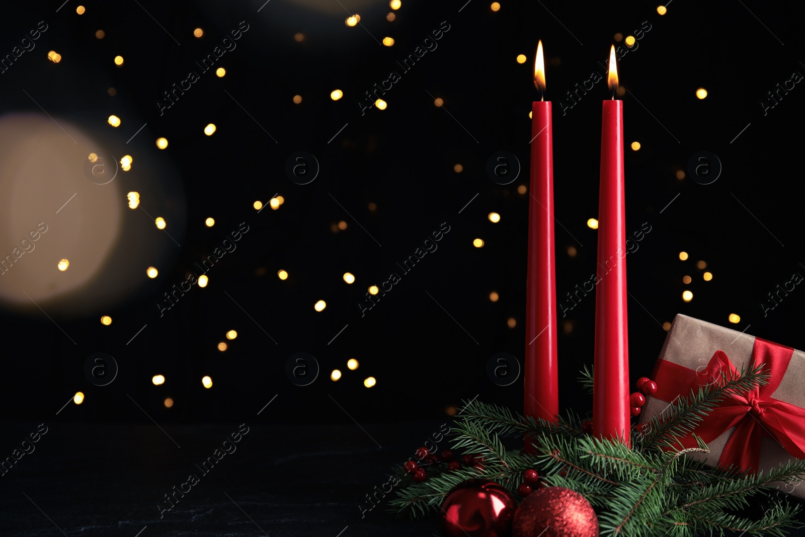 Photo of Burning candles, gift box and festive decor on dark table against blurred Christmas lights. Space for text