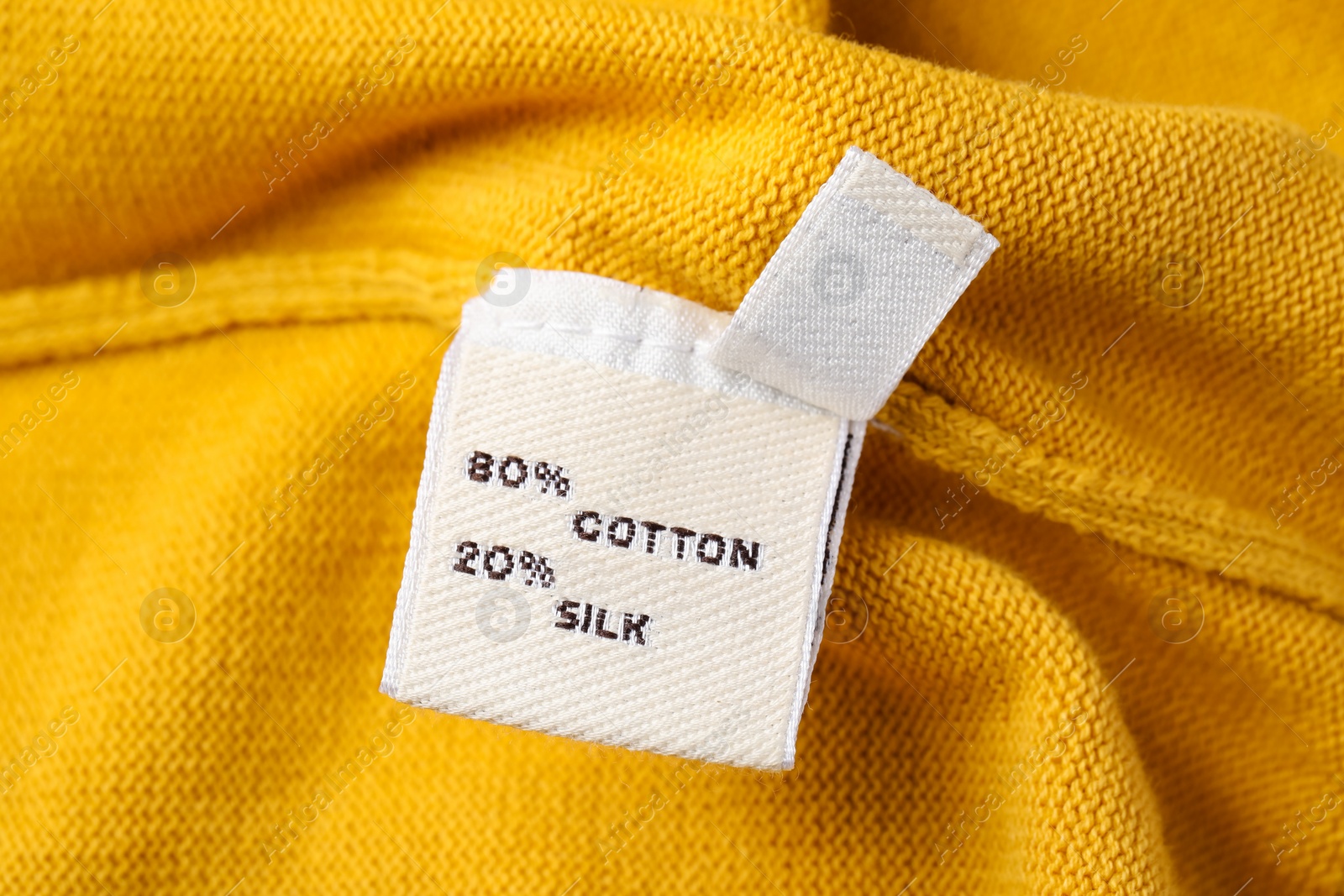 Photo of Clothing label on beautiful yellow garment, closeup
