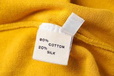 Clothing label on beautiful yellow garment, closeup