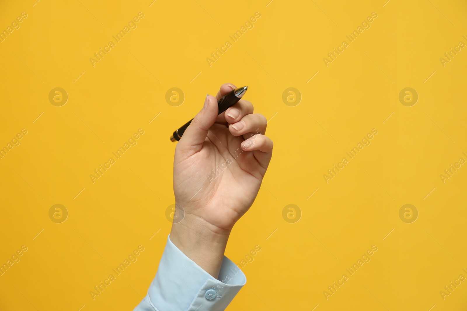 Photo of Left-handed woman holding pen on yellow background, closeup