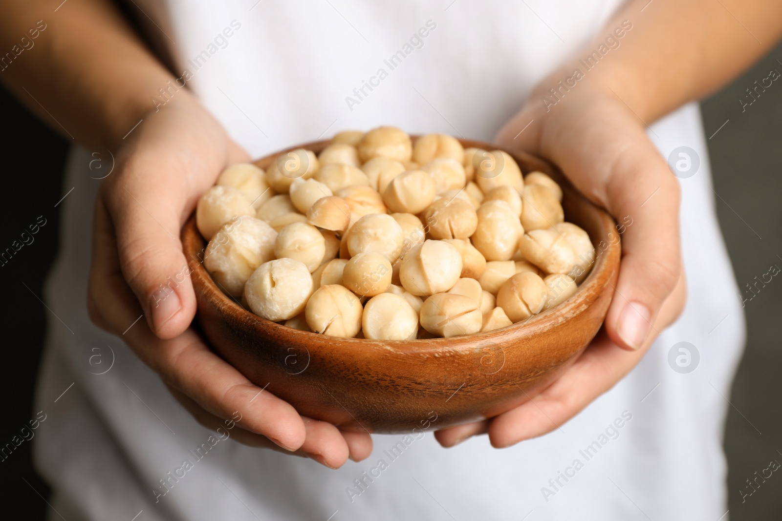 Photo of Woman holding bowl with shelled organic Macadamia nuts, closeup