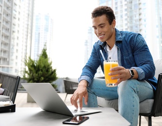 Photo of Portrait of handsome young African-American man with laptop and glass of juice in outdoor cafe