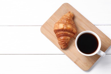 Photo of Tasty breakfast. Cup of coffee and croissant on white wooden table, top view. Space for text