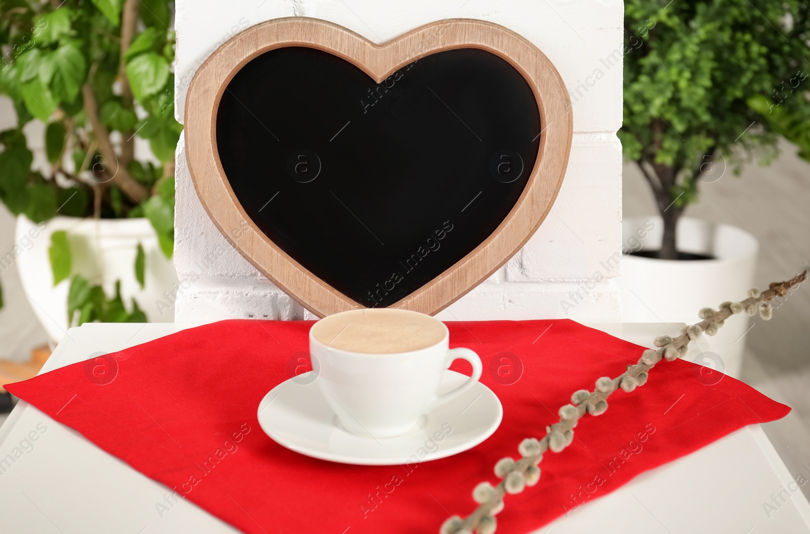 Photo of Cup of coffee on napkin near heart shaped chalkboard indoors