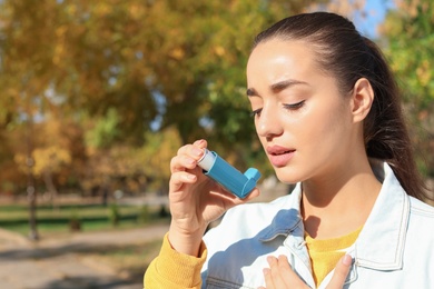 Photo of Young woman using asthma inhaler outdoors. Space for text