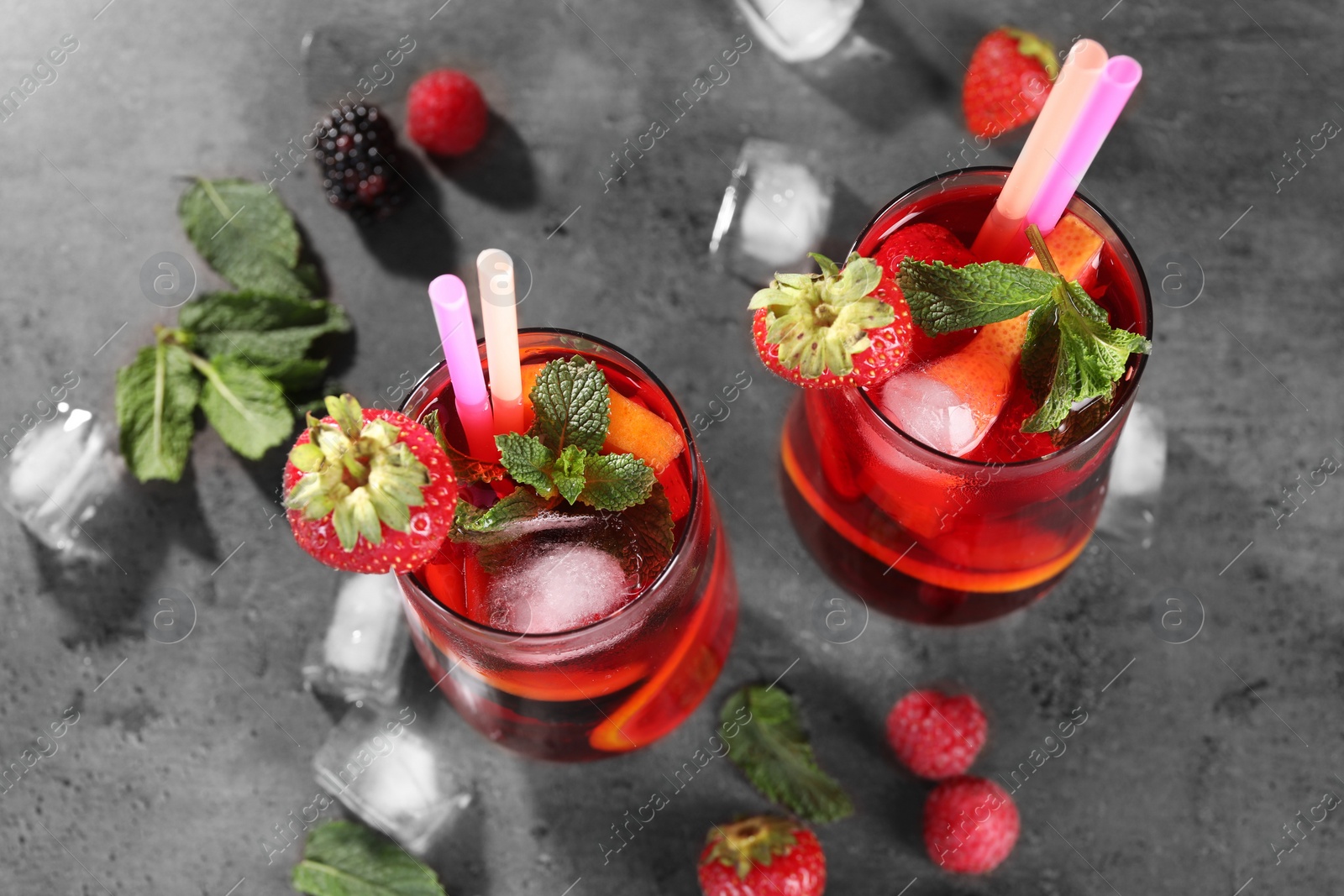 Photo of Delicious refreshing sangria, ice cubes and berries on grey table, above view