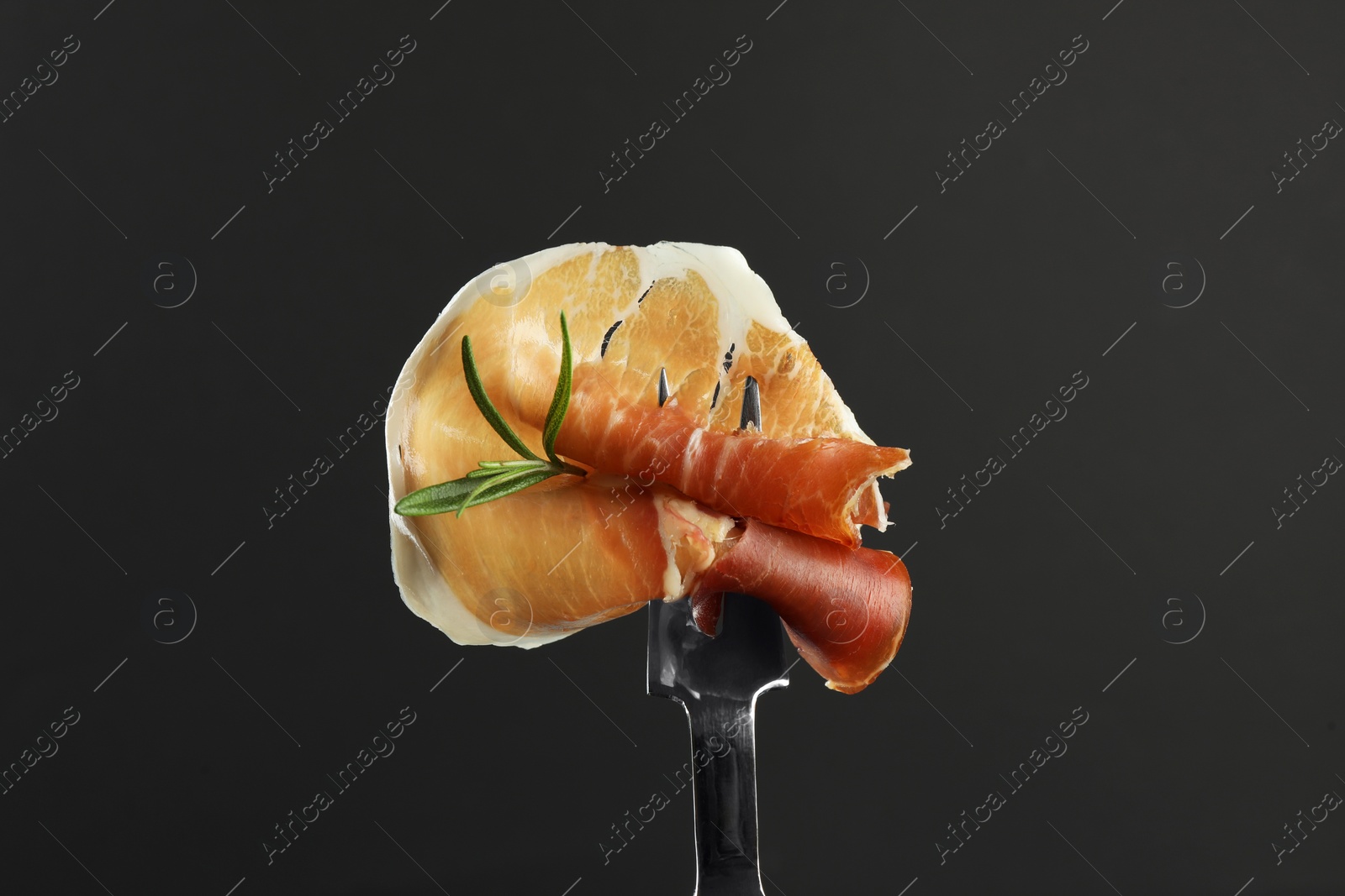 Photo of Fork with slice of tasty jamon and rosemary on black background, closeup