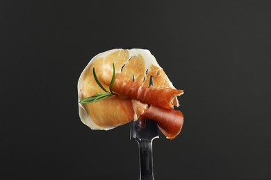 Fork with slice of tasty jamon and rosemary on black background, closeup