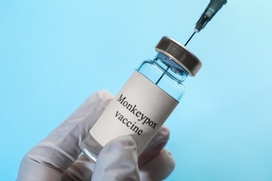Photo of Nurse filling syringe with monkeypox vaccine from vial on light blue background, closeup