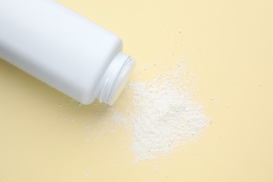 Photo of Bottle and scattered dusting powder on beige background, top view. Baby cosmetic product