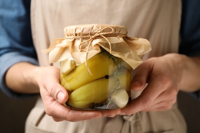 Woman holding jar with pickled peppers against dark background, closeup