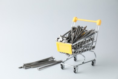 Metal nails in shopping cart on light grey background, space for text