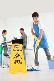 Photo of WET FLOOR sign and team of professional janitors in office