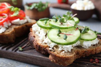 Photo of Delicious sandwich with cucumber, microgreens and cheese on wooden board, closeup
