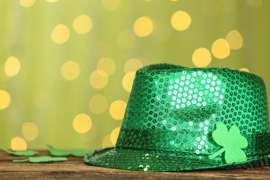 Green sequin hat with clover leaf on wooden table against blurred lights, space for text. St Patrick's Day celebration