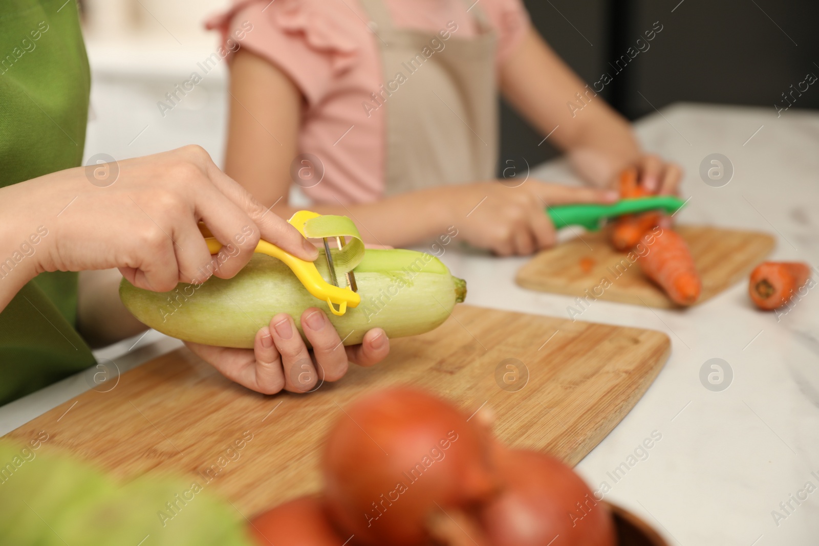 Photo of Mother and daughter peeling vegetables at table in kitchen, closeup