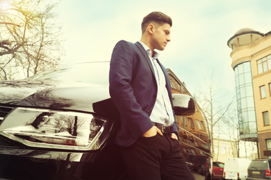 Handsome man near modern car outdoors, low angle view