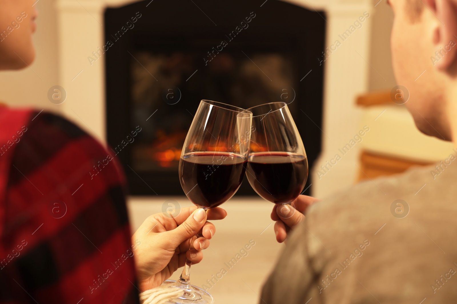 Photo of Lovely couple with glasses of wine resting together near fireplace at home, closeup