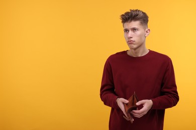 Photo of Upset man with empty wallet on yellow background. Space for text