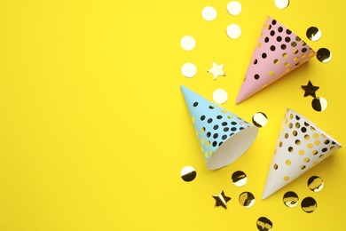 Photo of Bright party hats and shiny confetti on yellow background, flat lay. Space for text