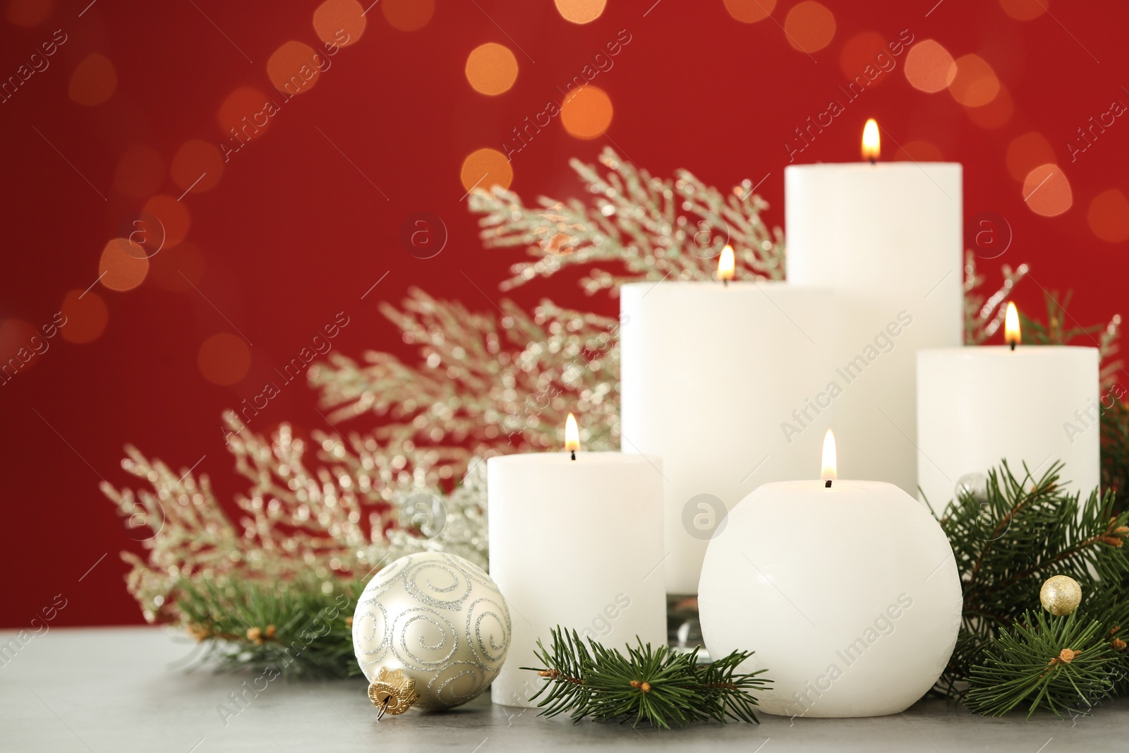 Photo of Burning white candles and Christmas decor on table against red background with bokeh effect