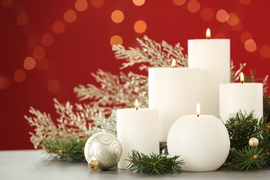 Burning white candles and Christmas decor on table against red background with bokeh effect