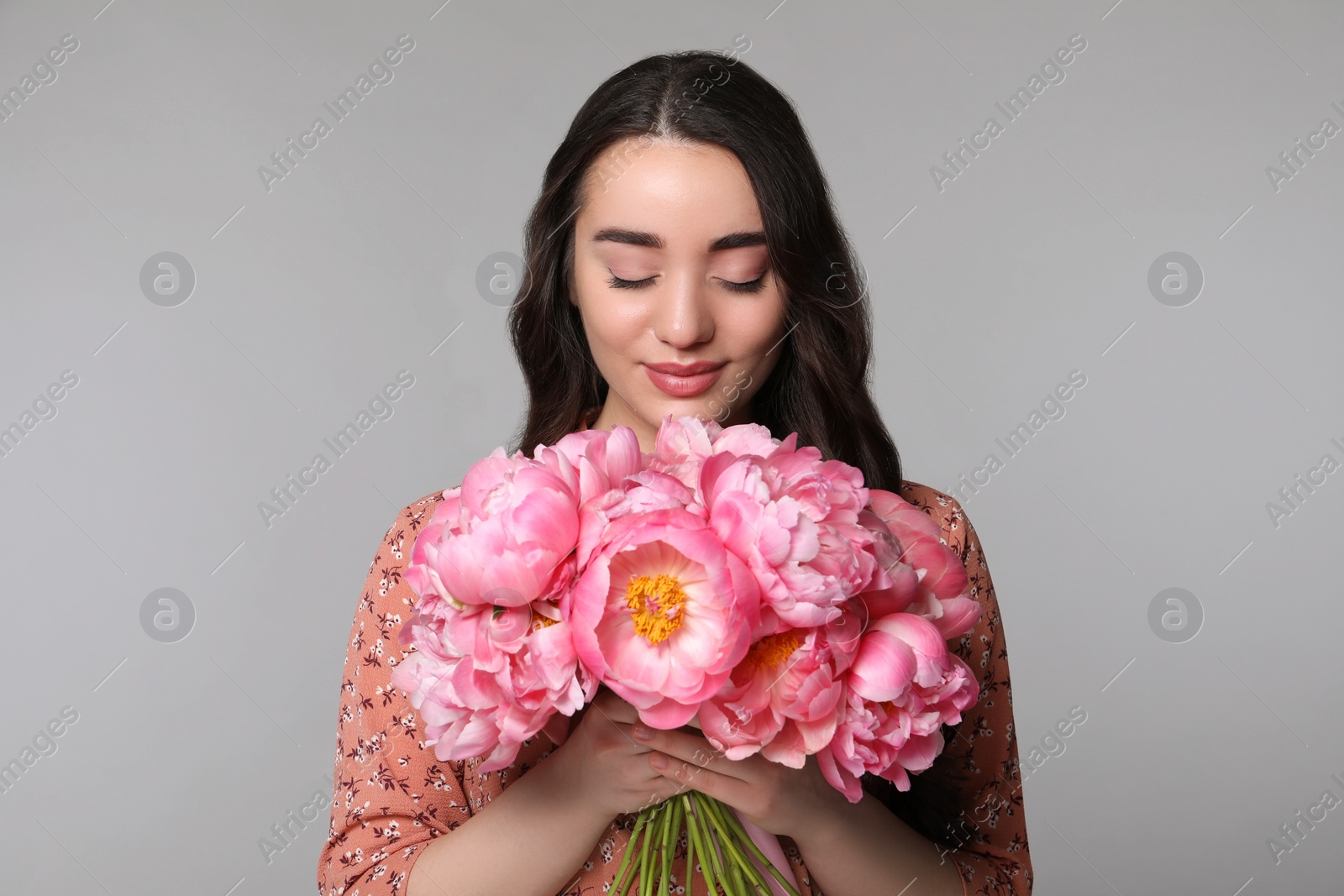 Photo of Beautiful young woman with bouquet of peonies on light grey background