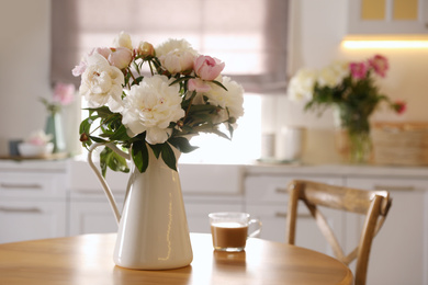 Photo of Beautiful peonies and cup of coffee on wooden table in kitchen