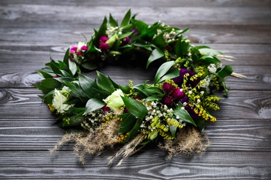 Photo of Beautiful wreath made of flowers and leaves on wooden table