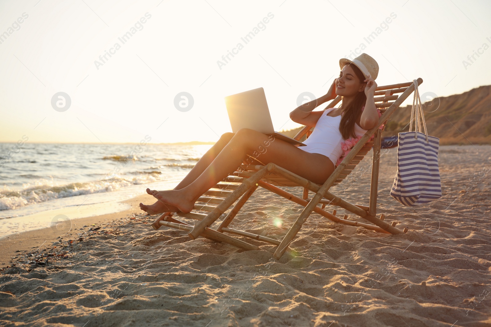 Photo of Young woman with laptop in deck chair on beach