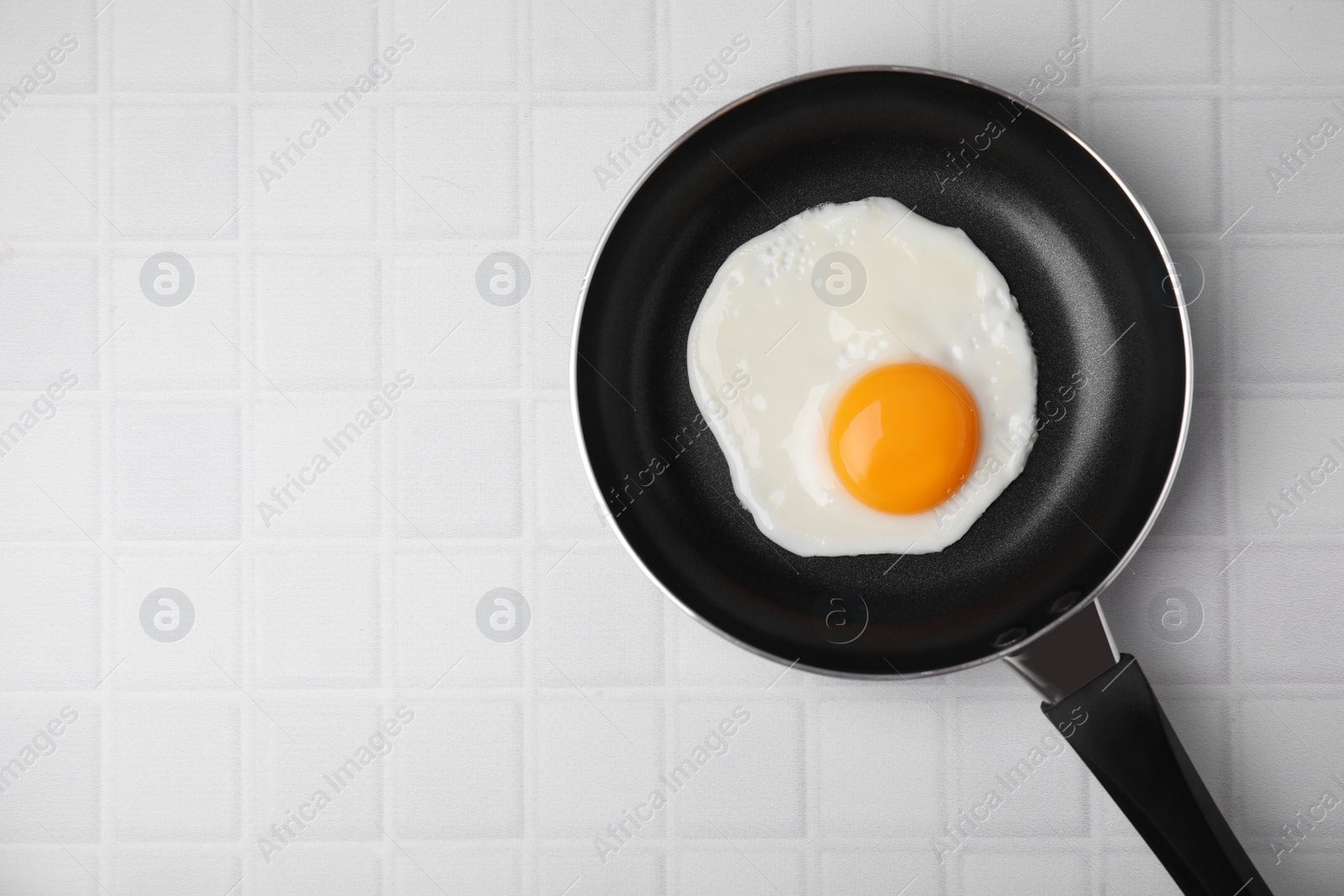 Photo of Tasty fried egg in pan on white table, top view. Space for text