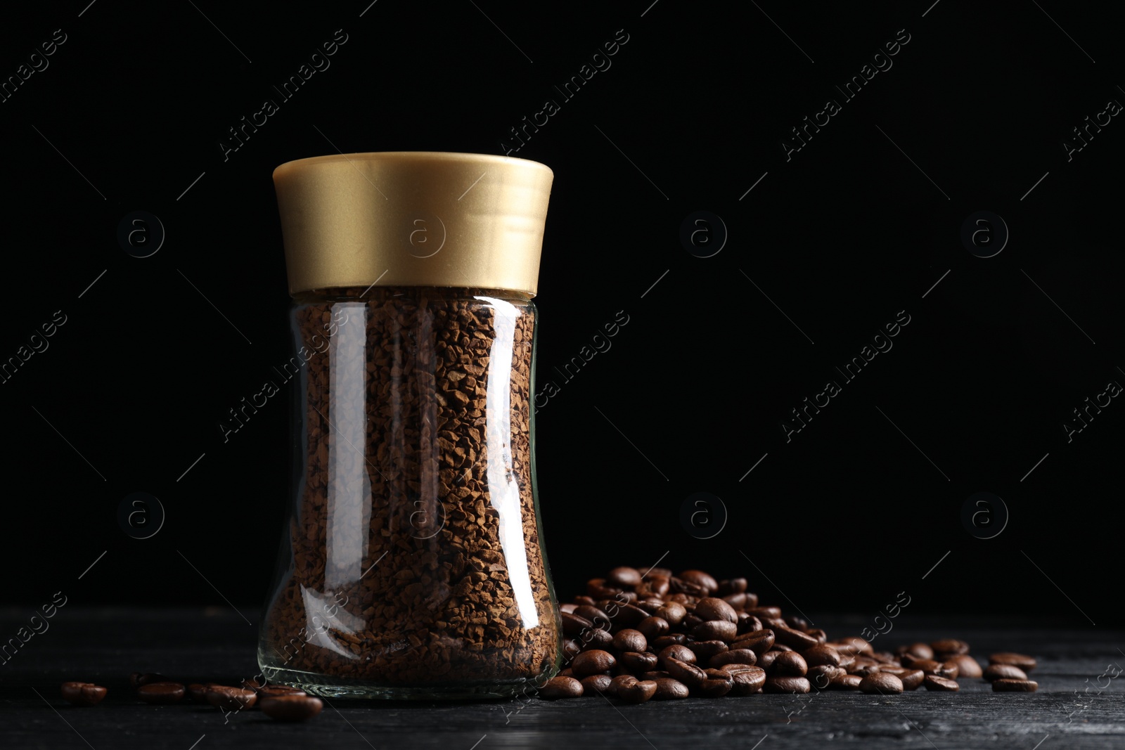 Photo of Glass jar with aromatic instant coffee and beans on black wooden table. Space for text