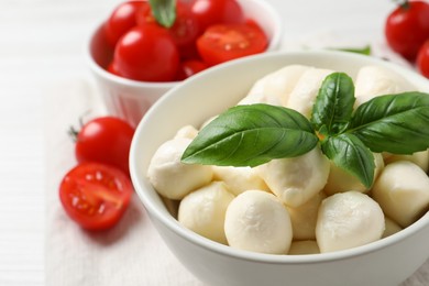 Photo of Delicious mozzarella balls and basil leaves in bowl on table, closeup