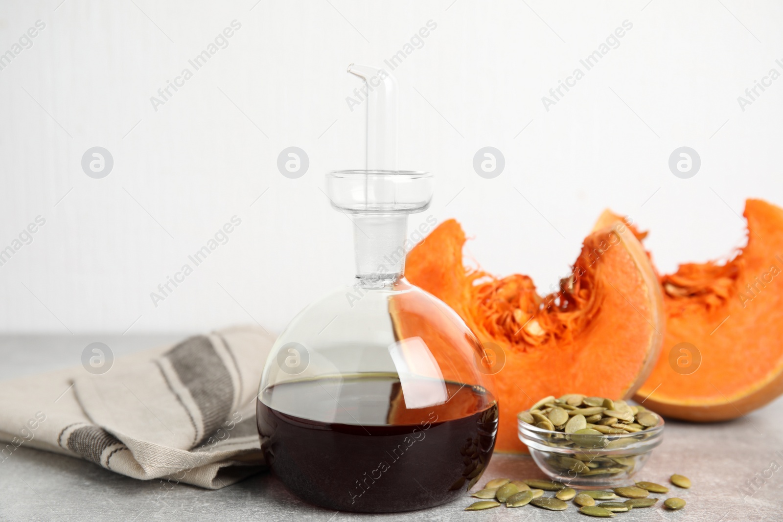 Photo of Laboratory glassware of oil with cut pumpkin and seeds on light grey table