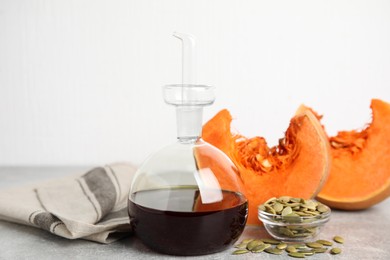 Photo of Laboratory glassware of oil with cut pumpkin and seeds on light grey table