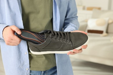 Man putting orthopedic insole into shoe indoors, closeup