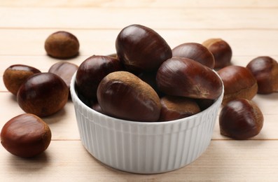 Sweet fresh edible chestnuts on light wooden table, closeup