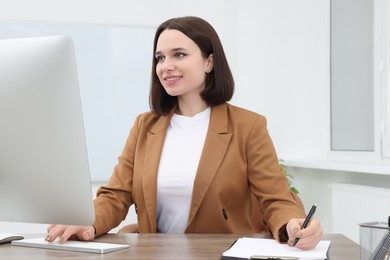 Photo of Happy young intern working with computer at table in modern office