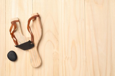 Slingshot with pebble on wooden background, top view. Space for text