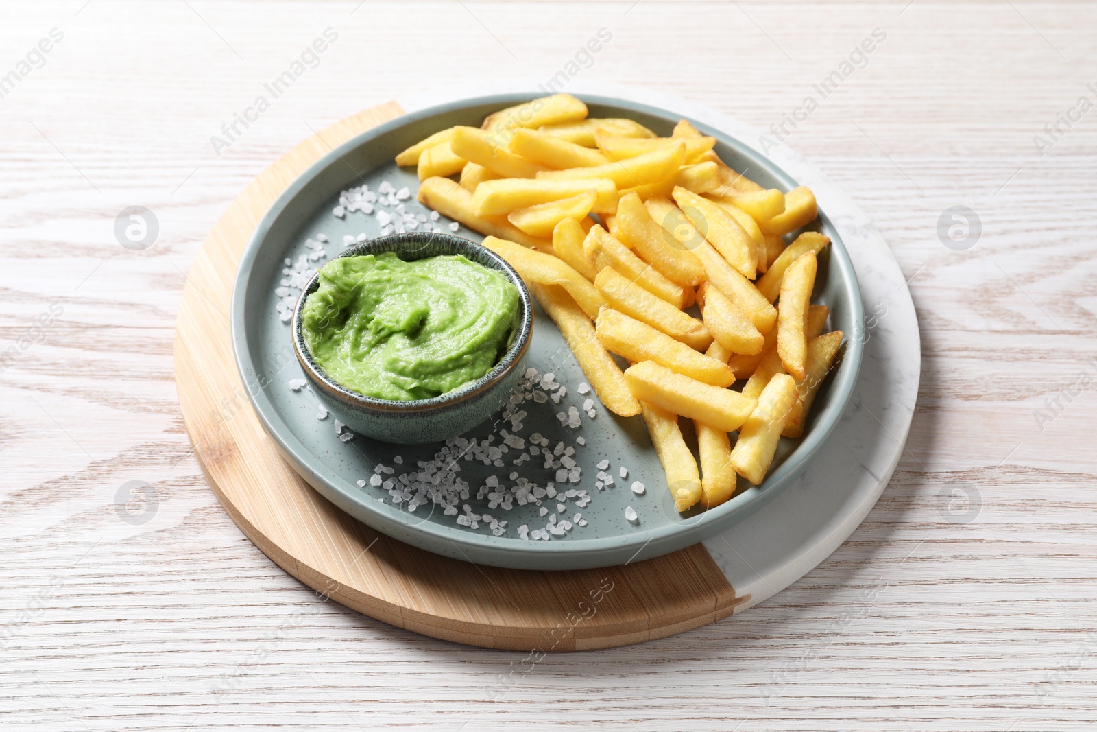 Photo of Tray with plate of french fries, salt and avocado dip on white wooden table