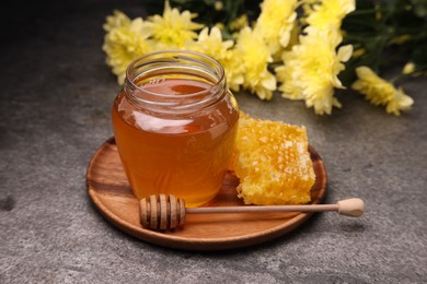 Photo of Sweet golden honey in jar, dipper and honeycomb on grey textured table
