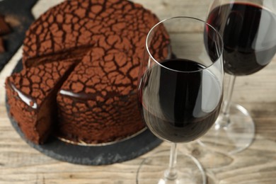 Photo of Delicious chocolate truffle cake and red wine on wooden table, closeup