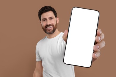 Happy man holding smartphone with empty screen on brown background