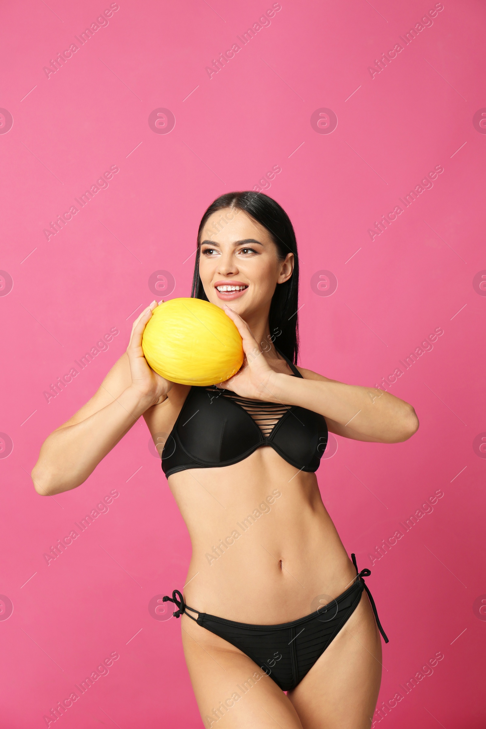 Photo of Beautiful young woman in black bikini with melon on pink background