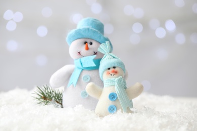 Snowman toys and branch of fir tree on snow against blurred festive lights. Christmas decoration