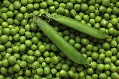 Pods on fresh raw green peas as background, top view