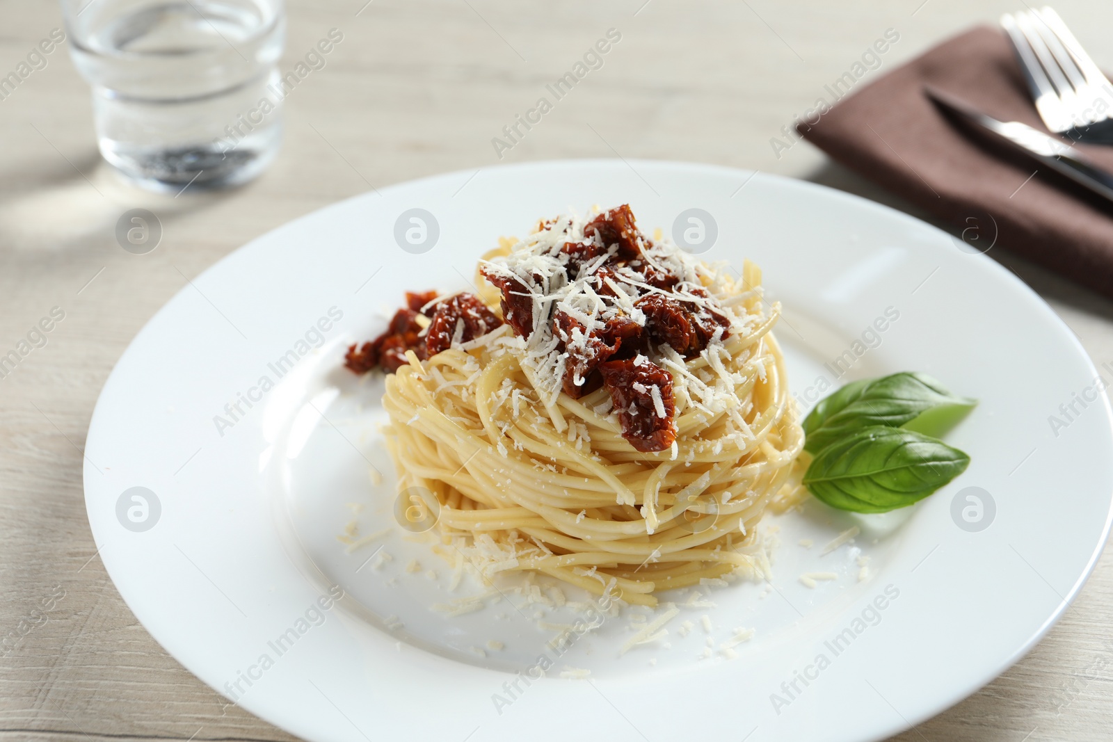 Photo of Tasty spaghetti with sun-dried tomatoes and parmesan cheese served on wooden table, closeup. Exquisite presentation of pasta dish